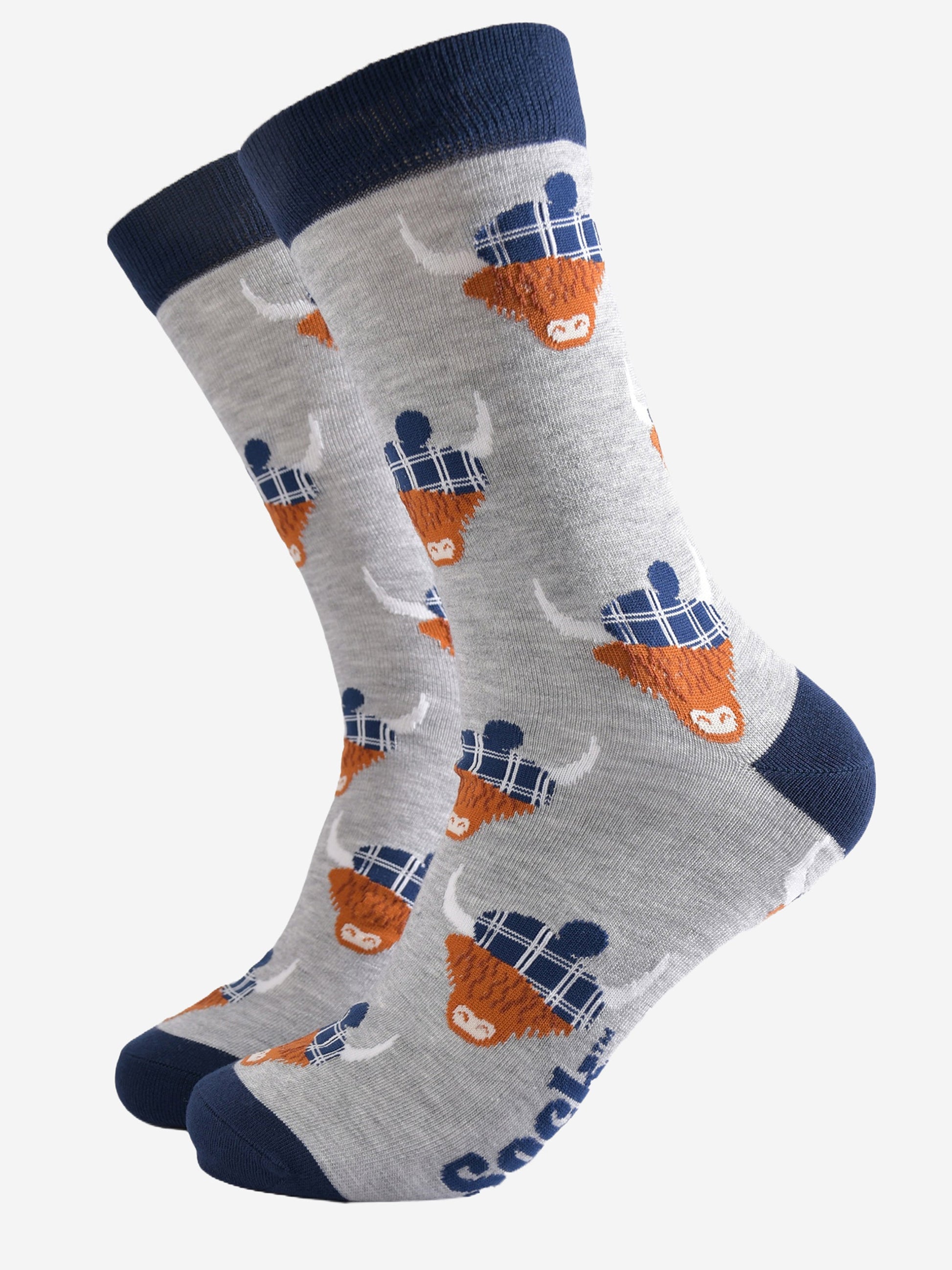 light grey socks with a navy blue heel, toe and cuff with an all over pattern of highland cows wearing tartan pom pom hats