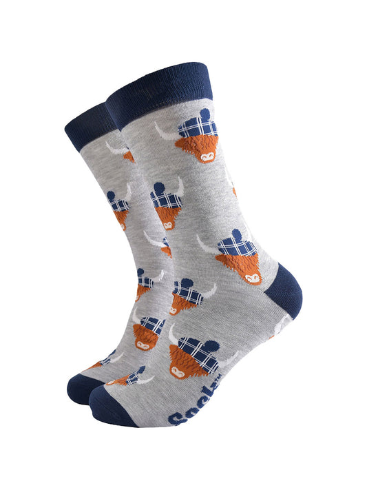 light grey socks with a navy blue heel, toe and cuff with an all over pattern of highland cows wearing tartan pom pom hats