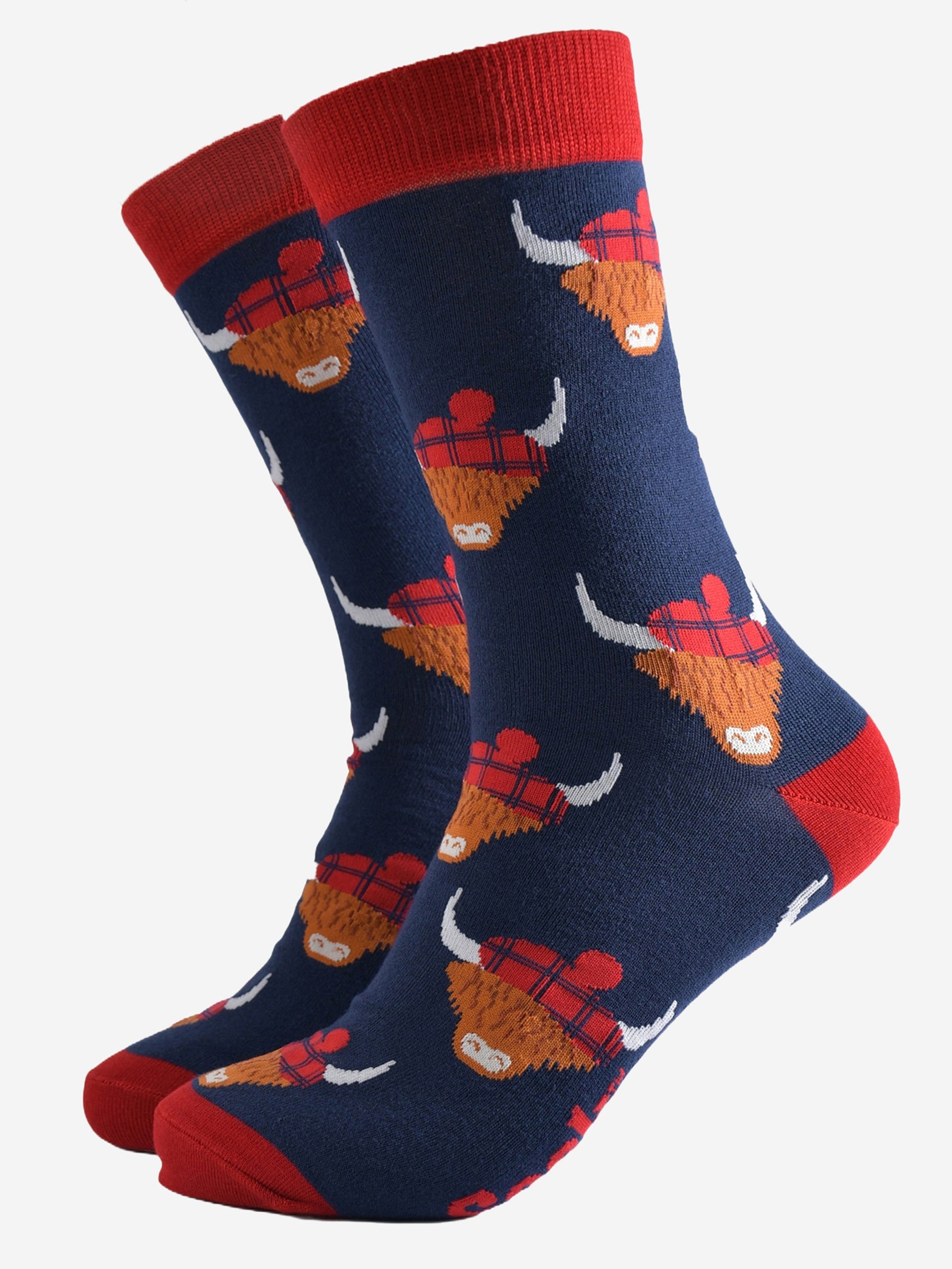 navy blue socks with red heel, toe and cuff with an all over pattern of highland cows wearing tartan pom pom hats