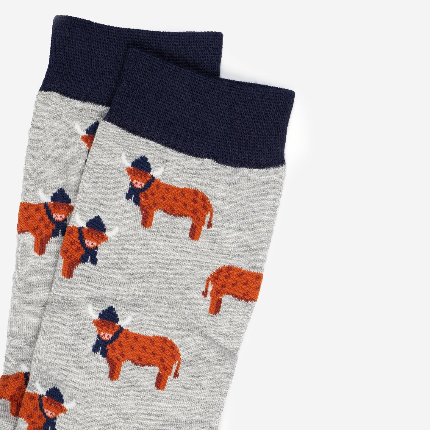 close up of the orange highland cows on the socks, the cows are standing up and they are designed to look like they have long hair, they are also wearing navy blue winter hats and scarves