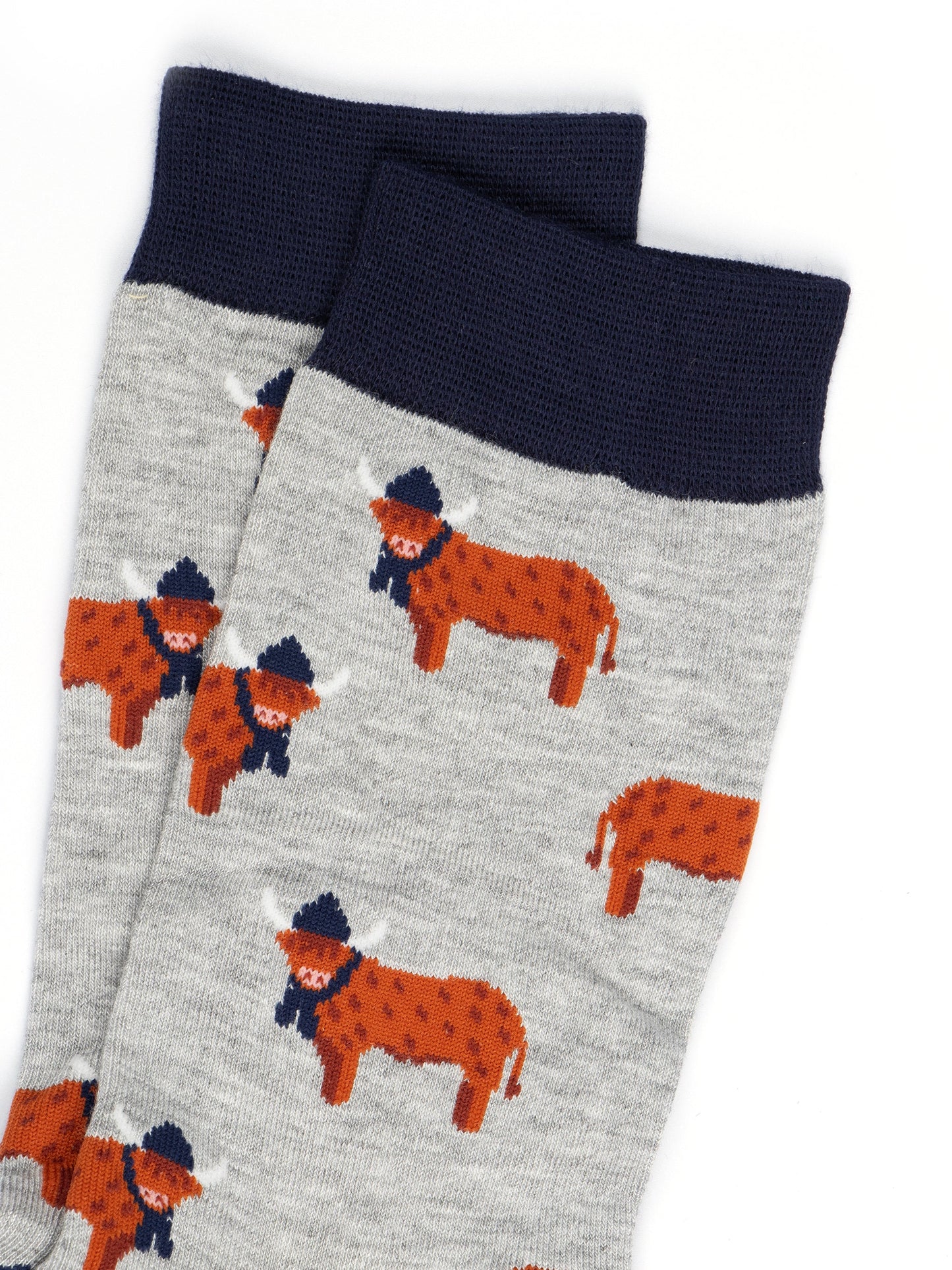 close up of the orange highland cows on the socks, the cows are standing up and they are designed to look like they have long hair, they are also wearing navy blue winter hats and scarves