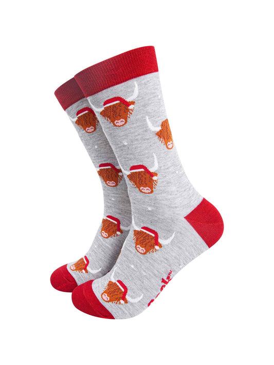 light grey socks with a red heel, toe and cuff with an all over pattern of highland cows wearing santa hats