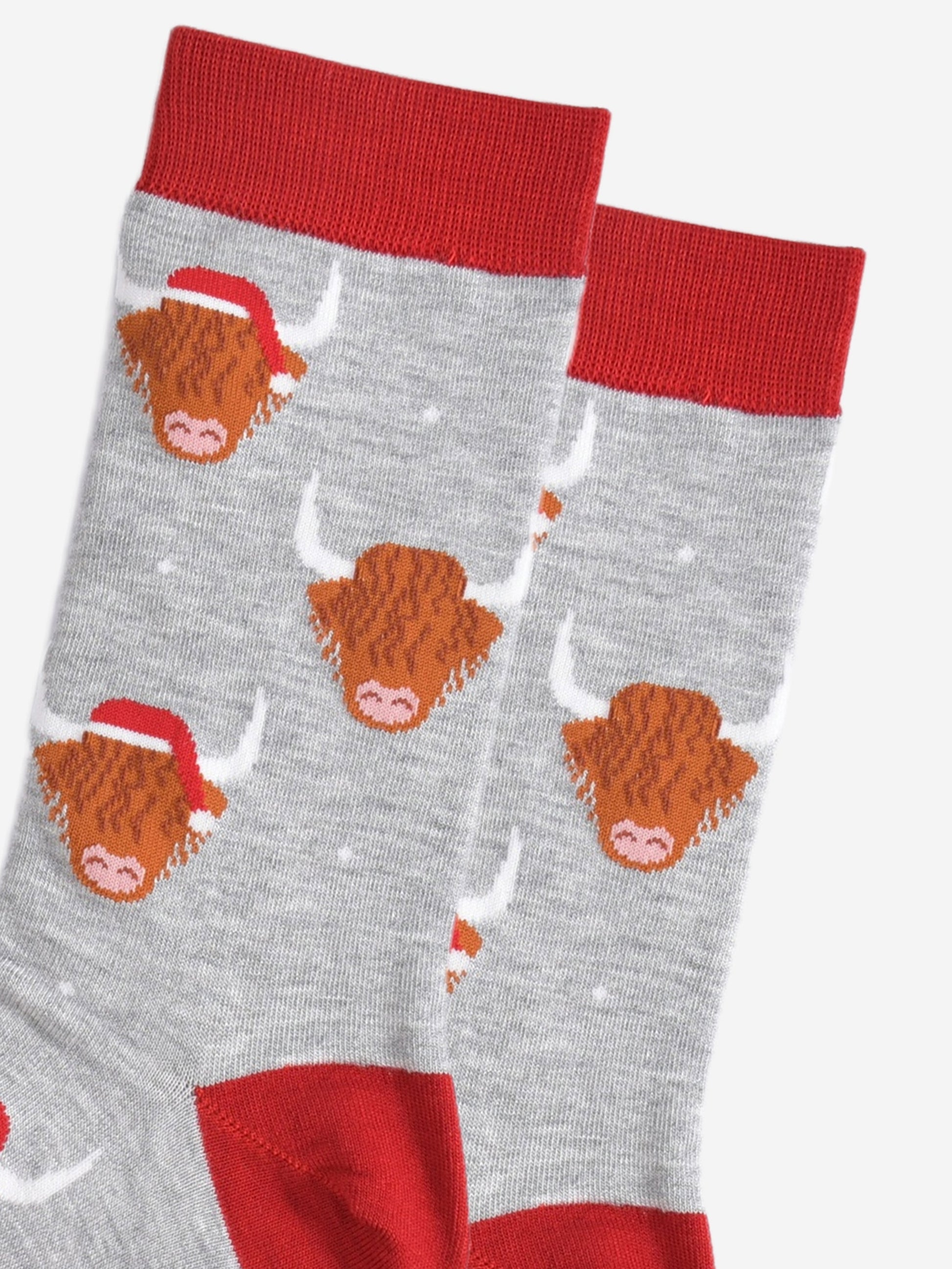 close up of the socks, showing the highland cow pattern where some of the cows are wearing santa hats, there is also a subtle white snowflake pattern on the socks