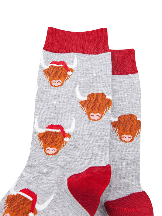 close up of the socks, showing the highland cow pattern where some of the cows are wearing santa hats, there is also a subtle white snowflake pattern on the socks