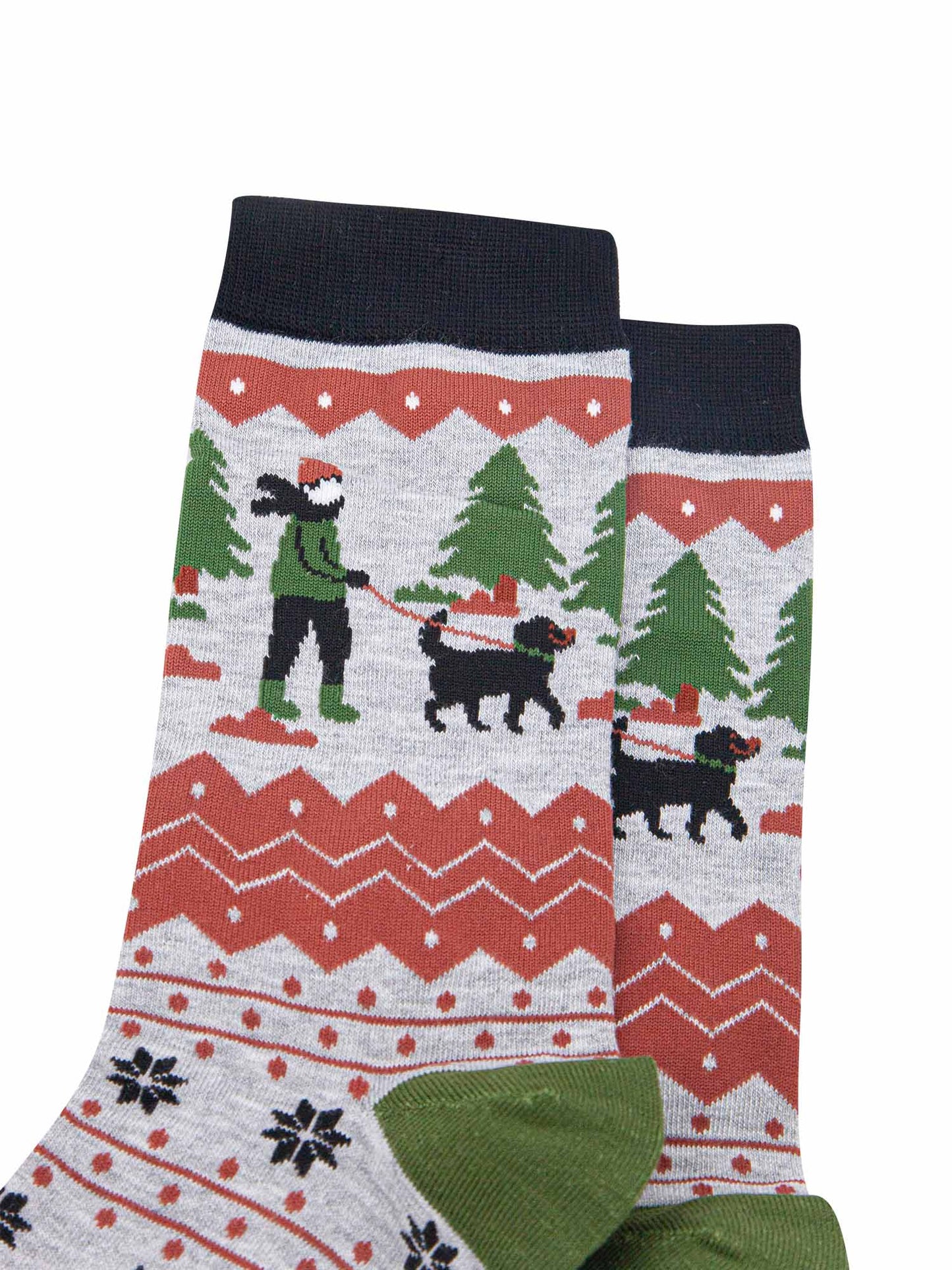close up of the dog walker on the ankle of the socks. there is a black fog wit a green collar and red leash. the dog walker is wearing a green coat and boots, black trousers and coral pink winter hat in keeping with the colour tones of the socks
