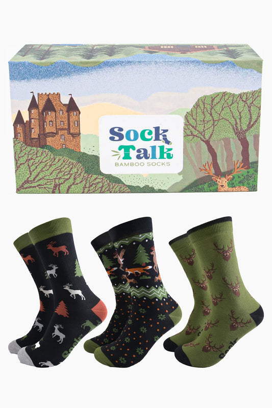 three pairs of woodland animal bamboo dress socks in a gift box designed to look like the scottish highlands. the box has a castle, stag and forest