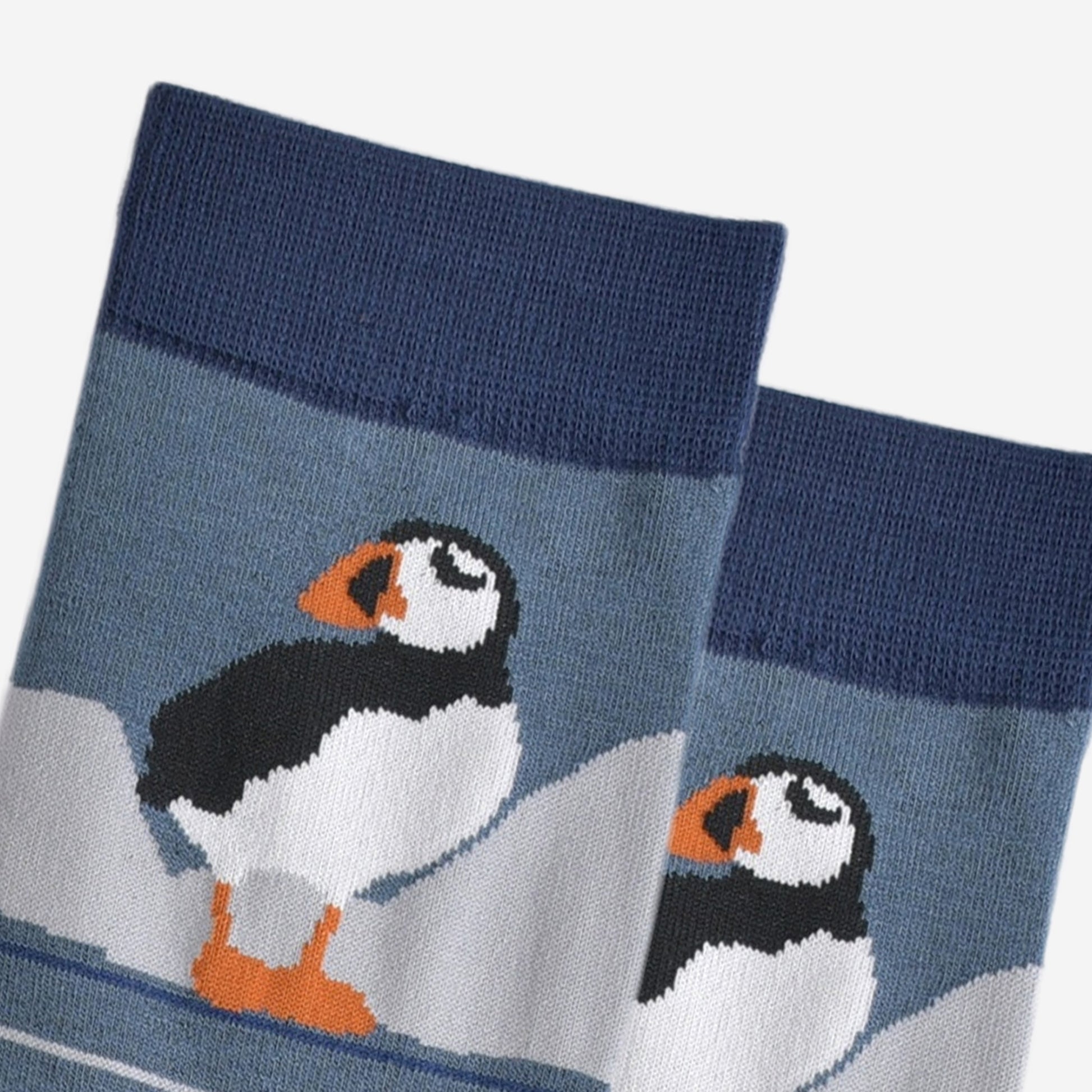 close up of the puffin, it is standing and has white cliffs behind it. 