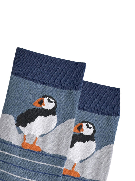 close up of the puffin, it is standing and has white cliffs behind it. 