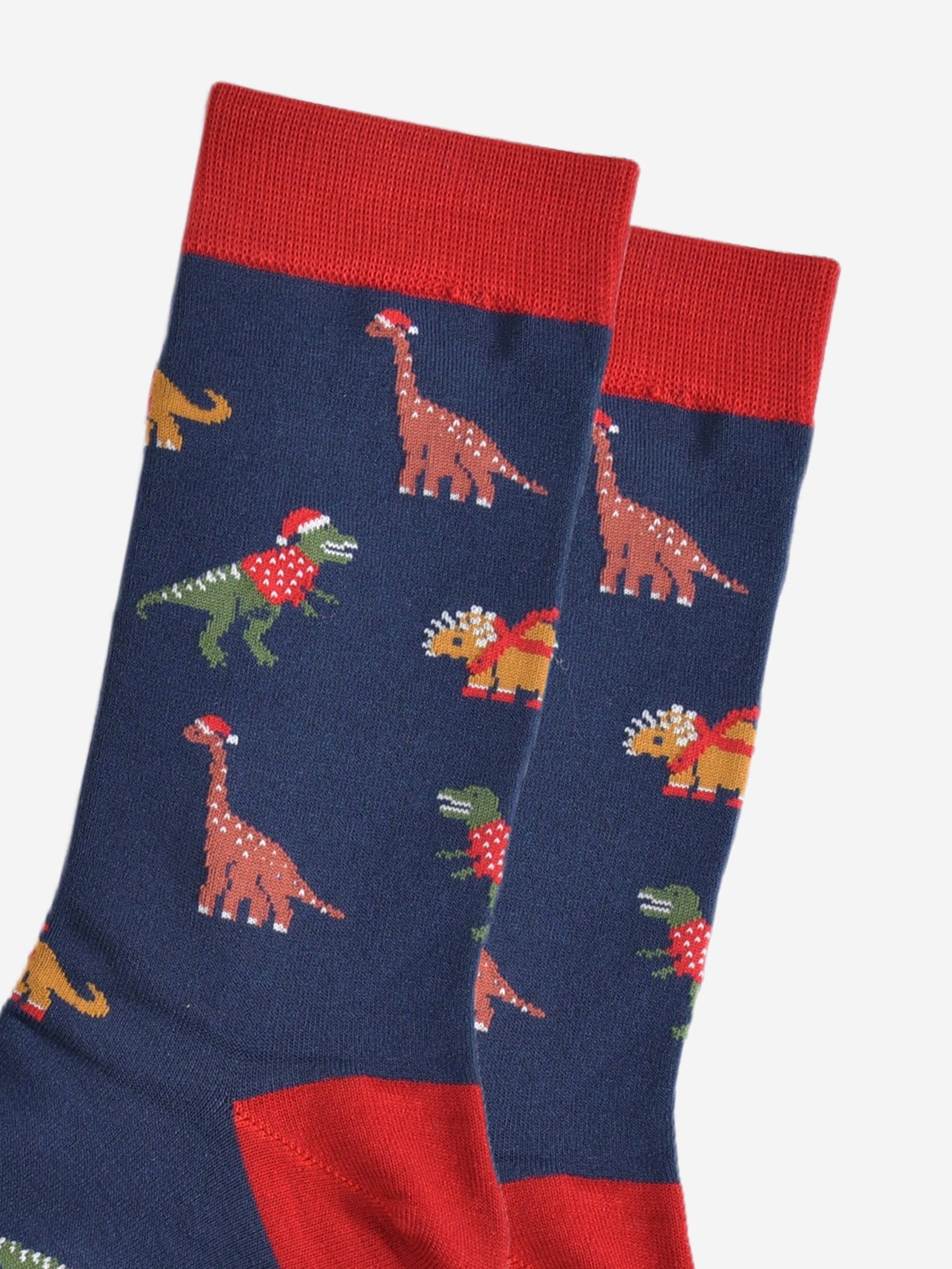 close up of the dinosaur design on the socks, t-rex, triceratops and brontosaurus are all wearing festive attire, santa hats and jumpers