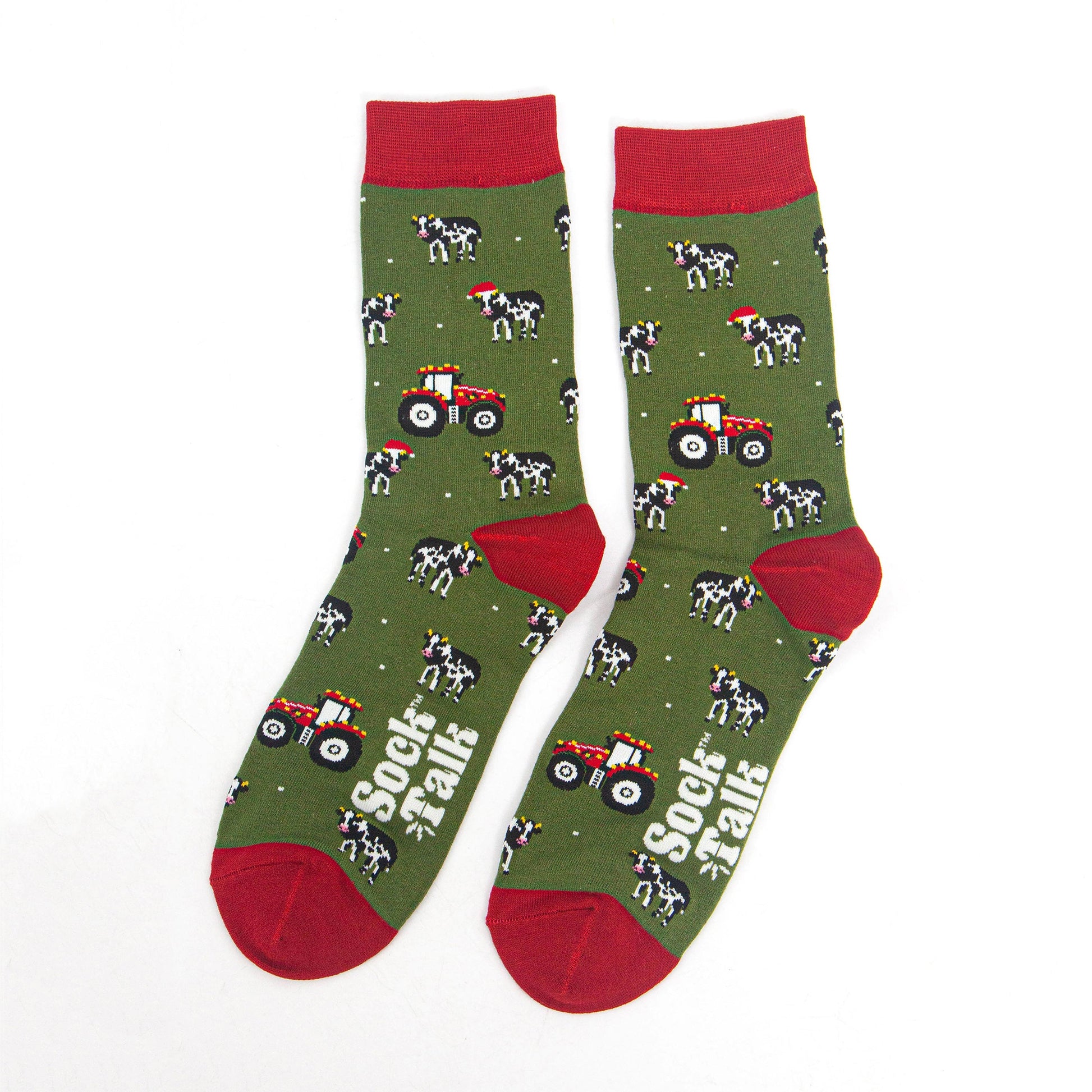 showing the tractor and cow socks laying flat, the cows are black and white with santa hats, the tractors are reed and have party lights on them. the toe, heel and cuff of the socks are red in contrast to the green body of the socks.