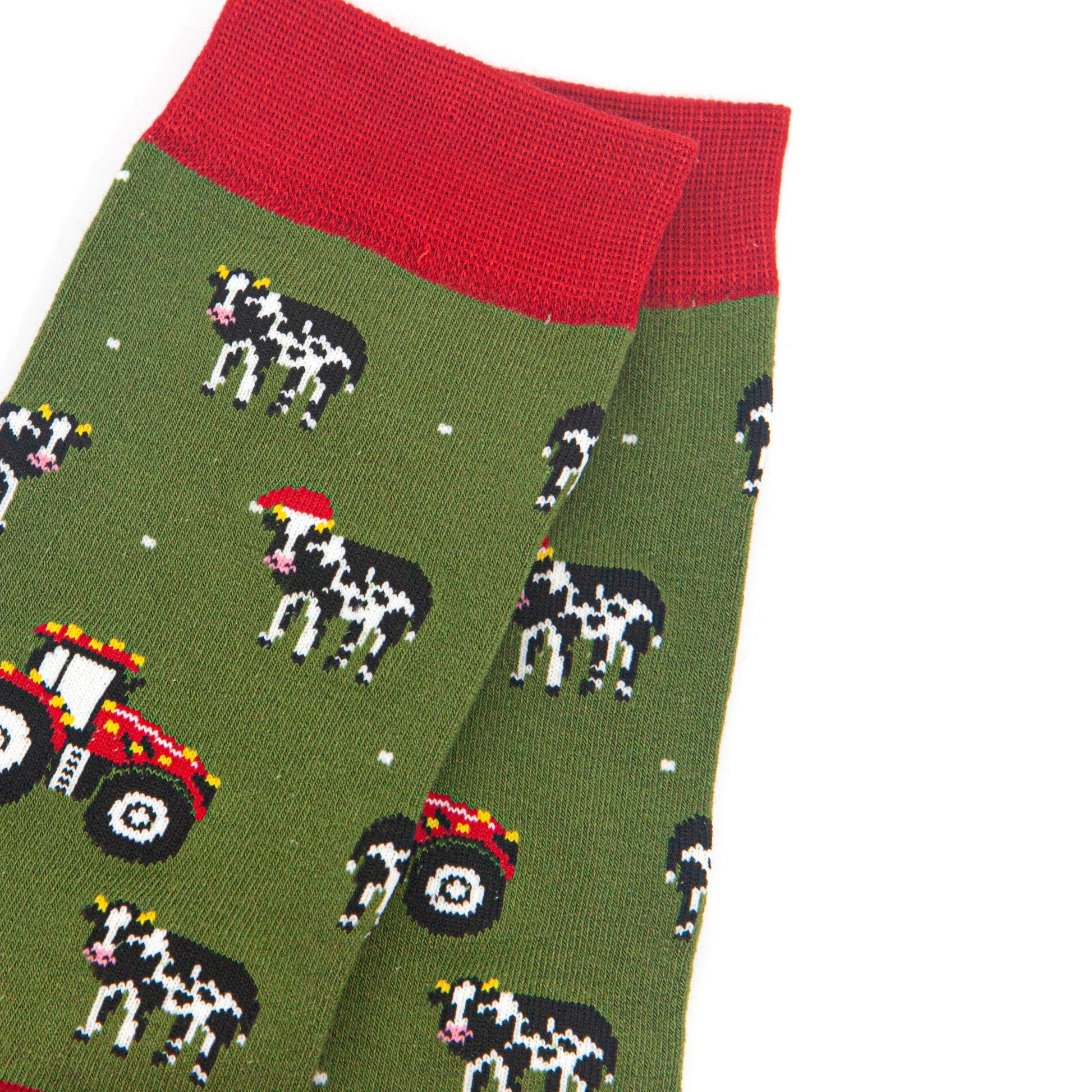 close up of the cow and tractor design on the socks, the cows are black and white, some are wearing santa hats. the tractors are red and have gold party lights on them. 