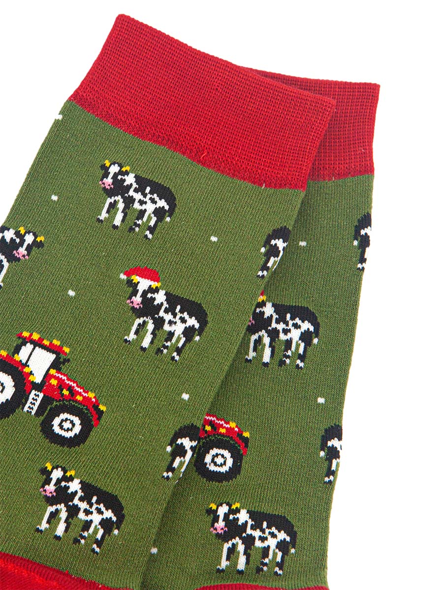 close up of the cow and tractor design on the socks, the cows are black and white, some are wearing santa hats. the tractors are red and have gold party lights on them. 