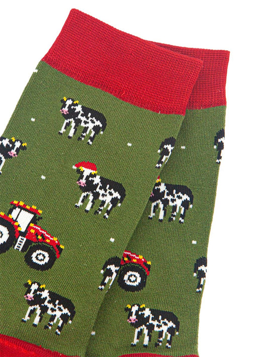 close up of the cow and tractor design on the socks, the cows are black and white, some are wearing santa hats. the tractors are red and have gold party lights on them. 