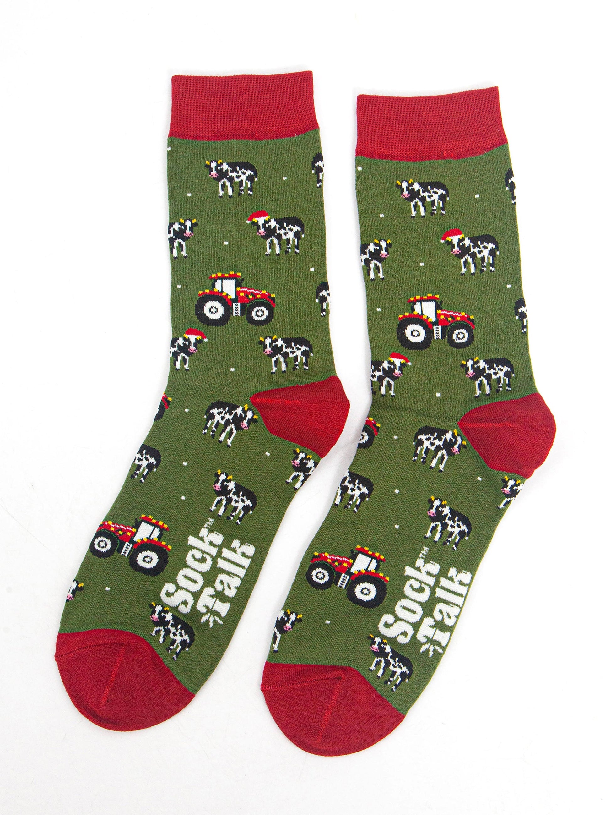showing the tractor and cow socks laying flat, the cows are black and white with santa hats, the tractors are reed and have party lights on them. the toe, heel and cuff of the socks are red in contrast to the green body of the socks.