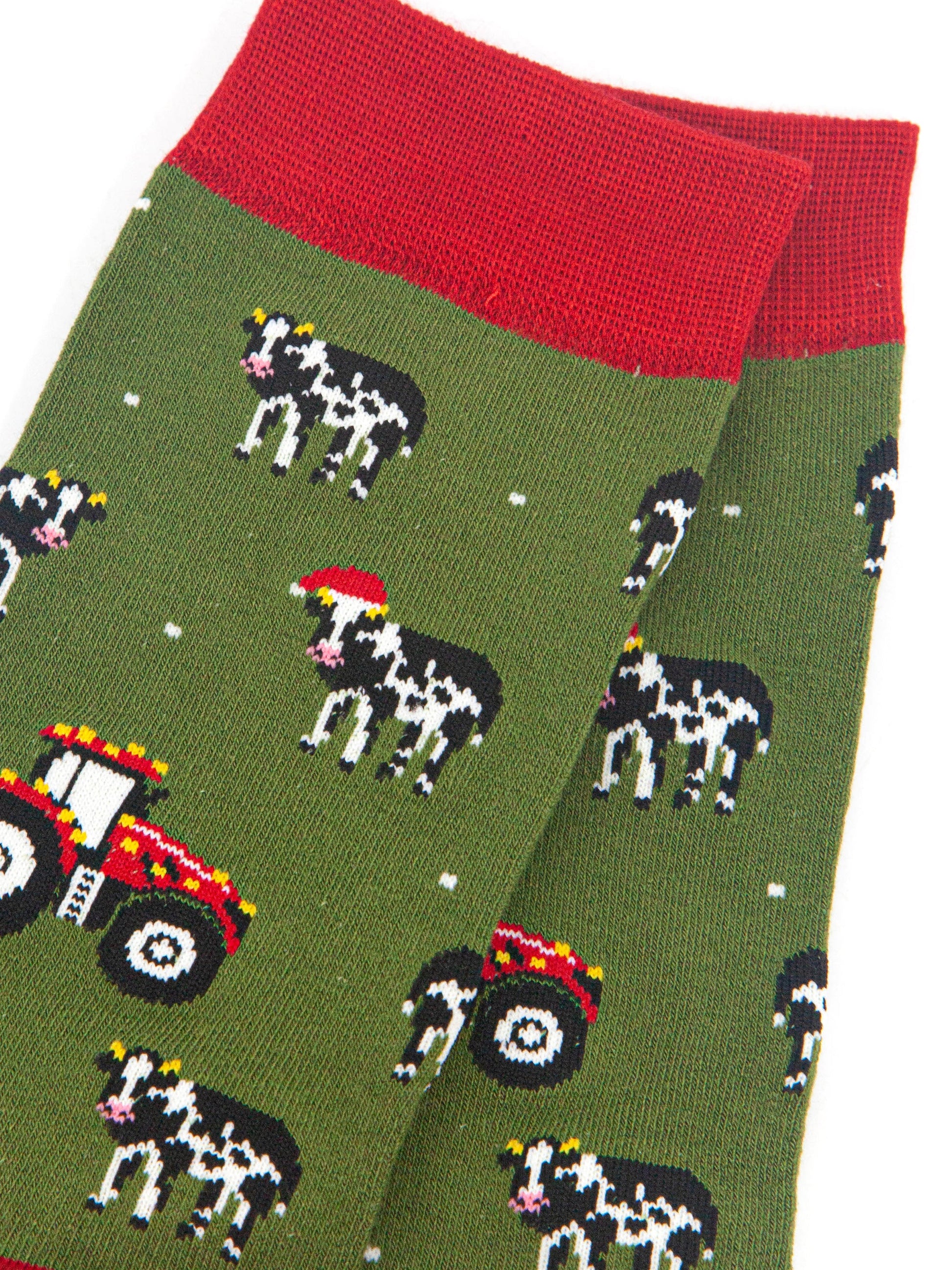 close up of the cow and tractor design on the socks, the cows are black and white, some are wearing santa hats. the tractors are red and have gold party lights on them. 