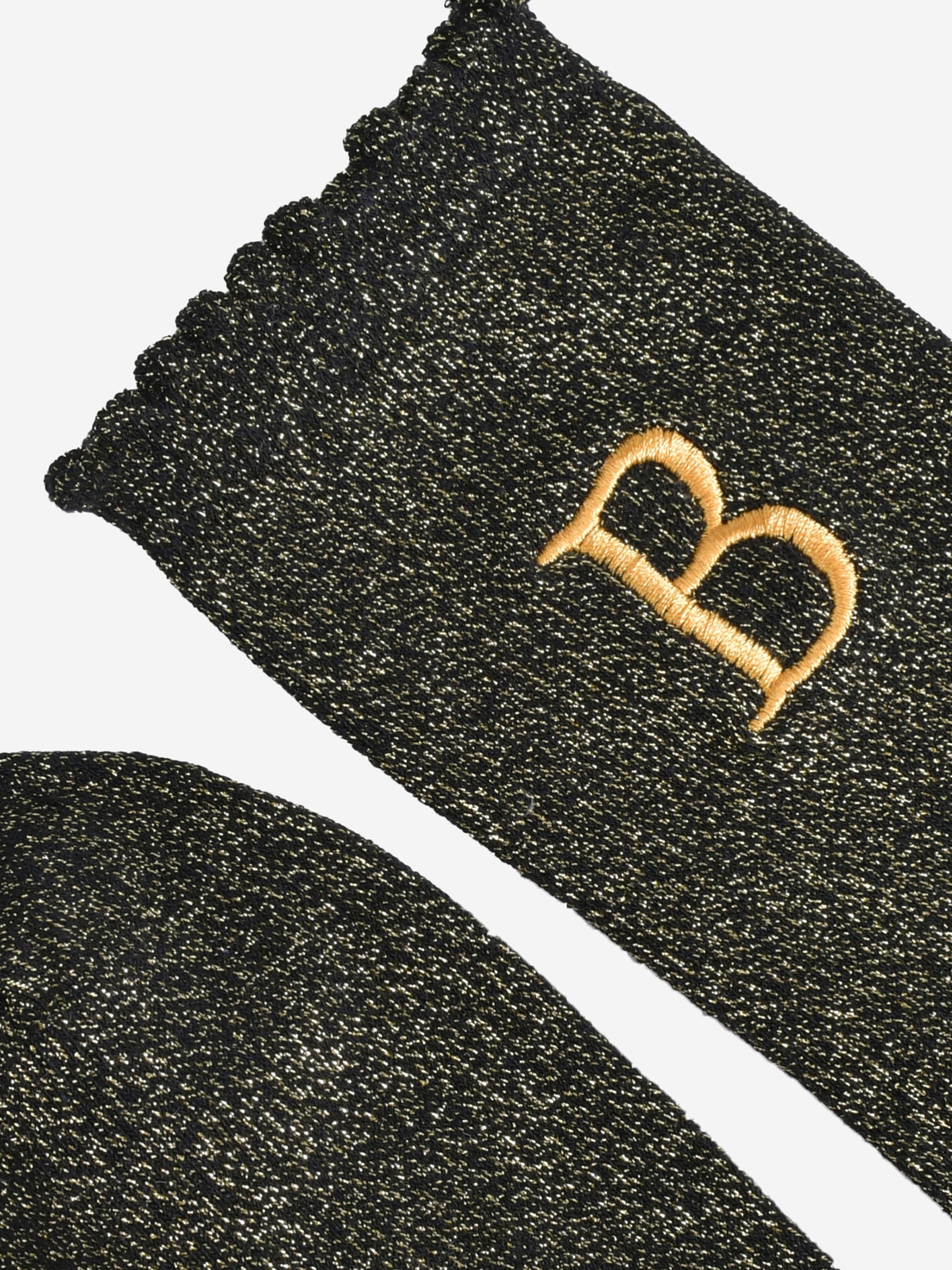 close up of the scalloped cuff on the socks, the toe is the same black and gold as the rest of the socks