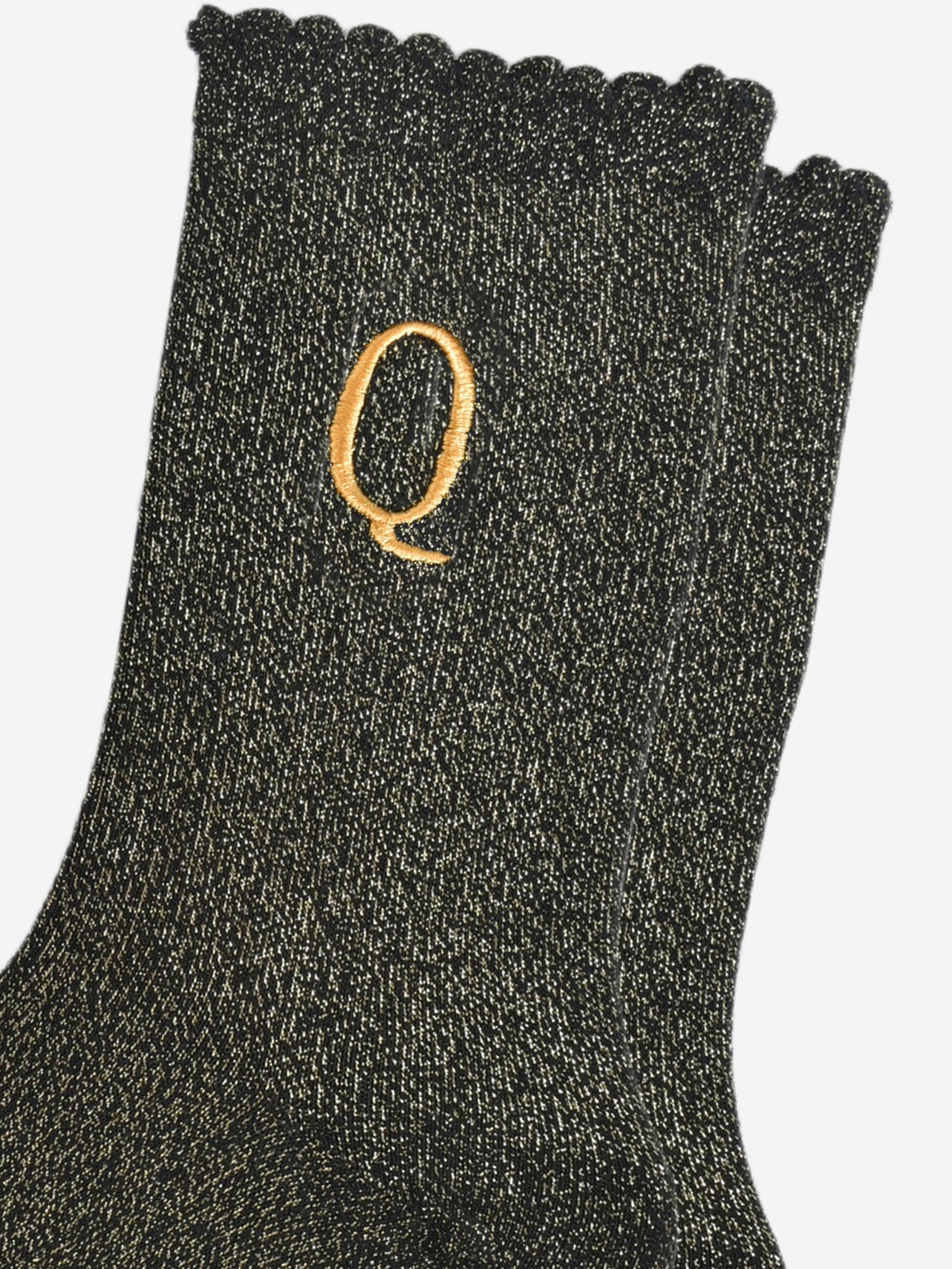close up of the gold embroidered capital letter q on the ankle of the socks