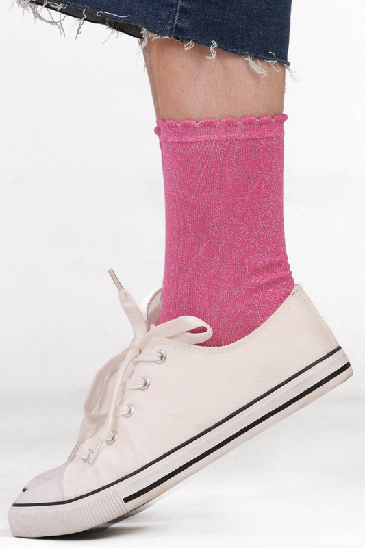 Women's model feet wearing pink cotton glitter socks with scallop edge. Wearing white trainers