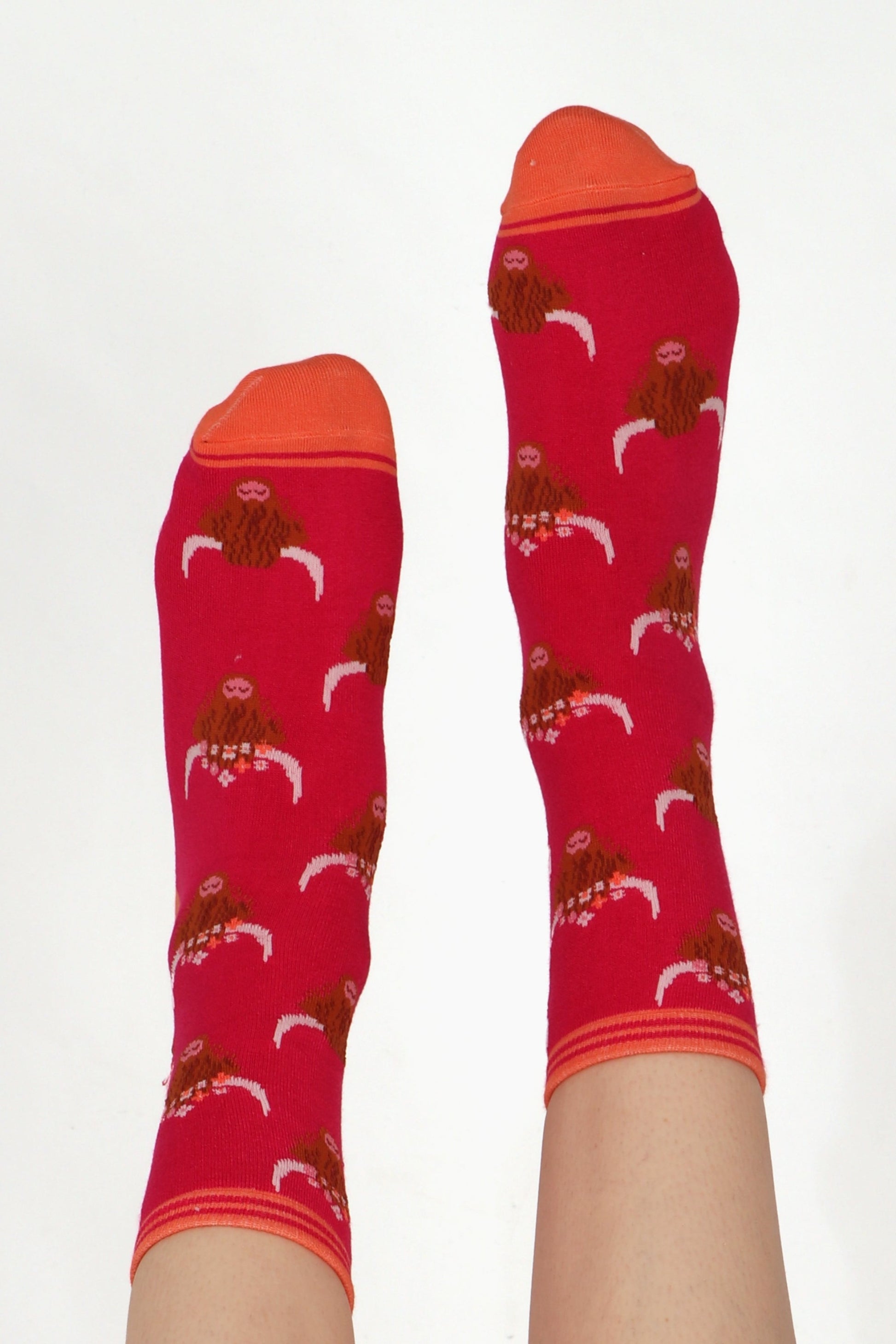 Ladies feet posed straight in the air wearing highland cow print socks. Cows are wearing flower crowns. Shows contrasting orange colour toe and cuff
