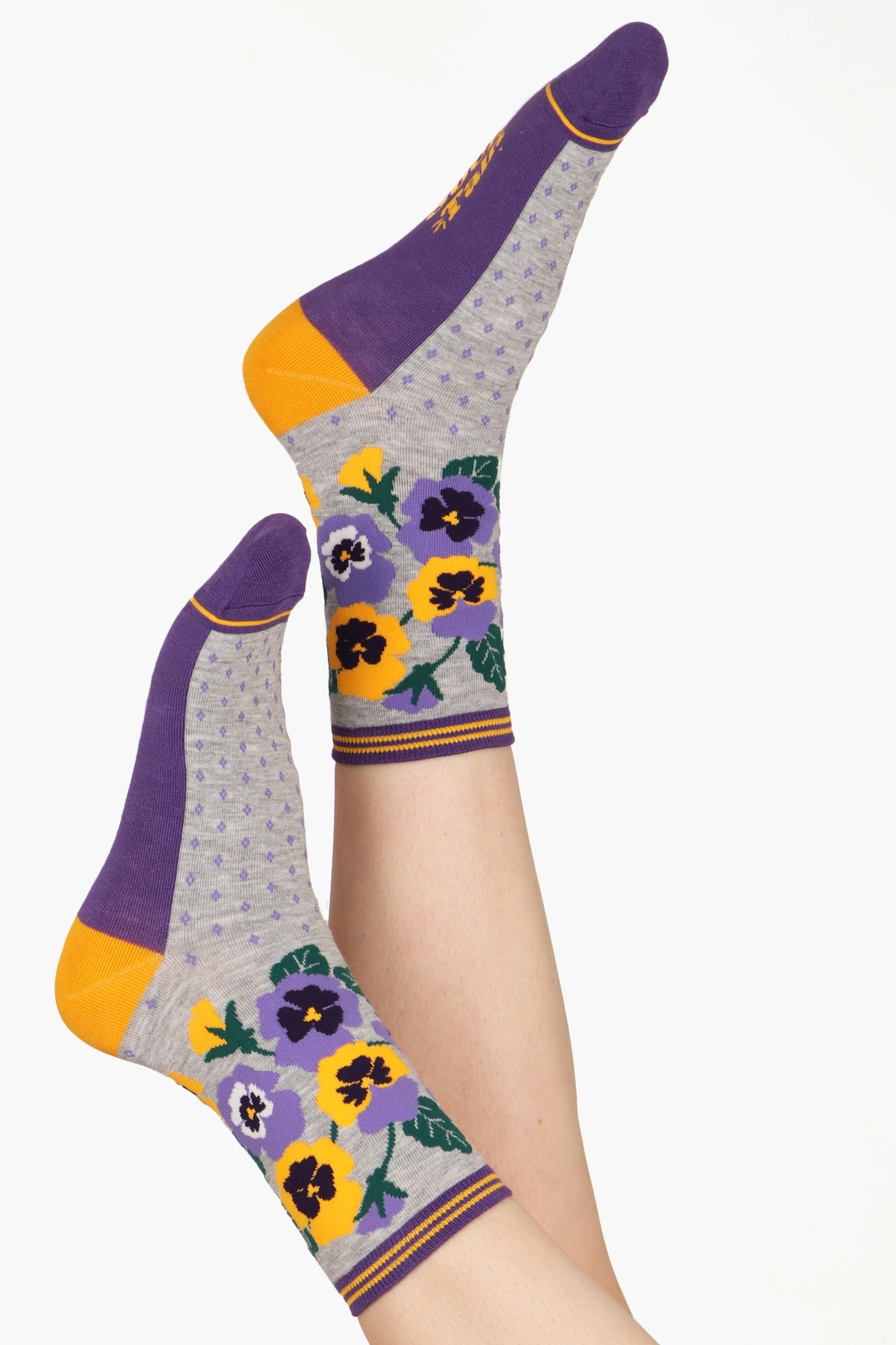 Ladies feet posed in the air wearing pansy floral print socks in grey, yellow and purple