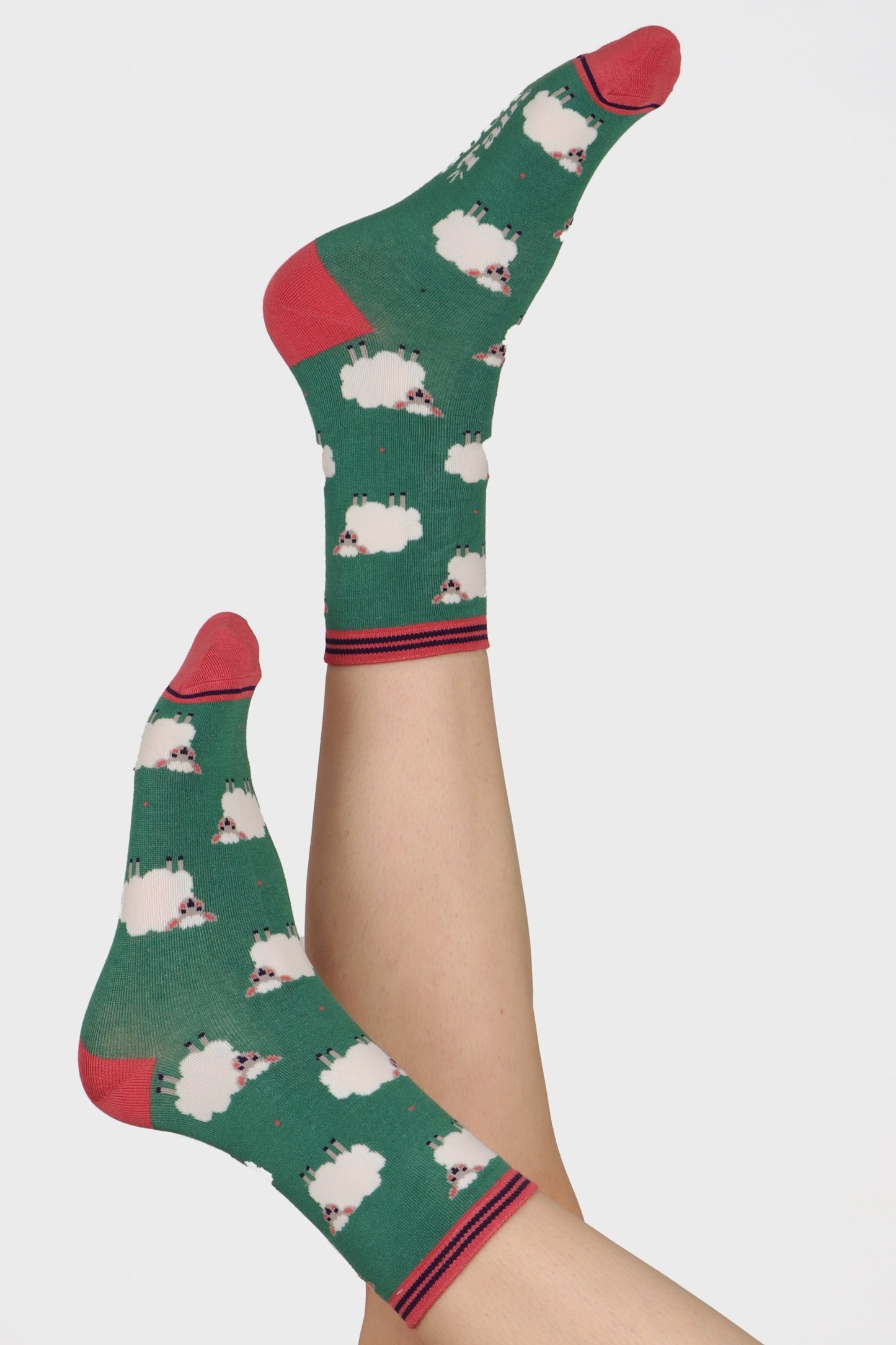 Ladies feet posed in the air wearing green base socks with spring sheep print. Contrasting heel toe and cuff in pink can be seen
