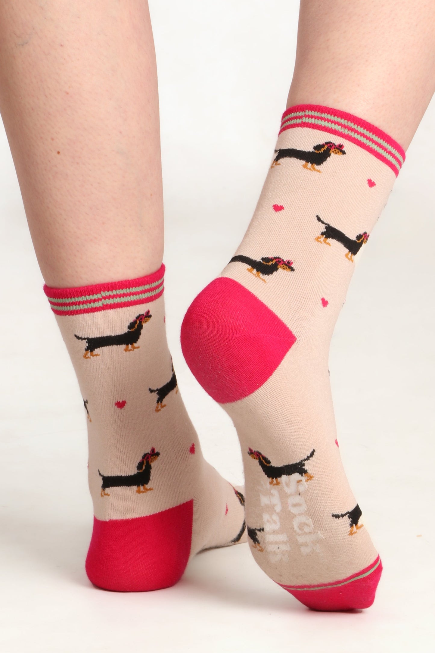 Ladies feet posed away from camera wearing sausage dog print bamboo socks. Image highlights sock talk logo on sole of sock and pink contrasting heel. Sausage dogs are wearing heart sunglasses