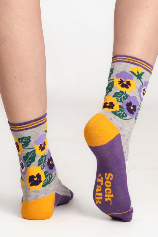 Ladies feet posed facing away froom camera wearing pansy floral print sock talk bamobbo socks in yellow and purple. Image shows yellow contrasting heel and sock talk logo on sole
