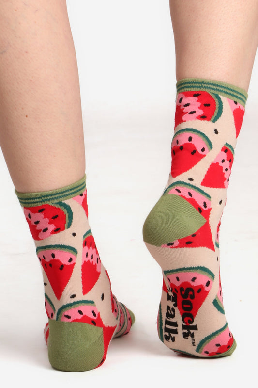 Ladies feet walking away from camera wearing watermelon fruit print bamboo socks. Image socks sock talk logo on sole of sock and highlights green contrasting heel detail