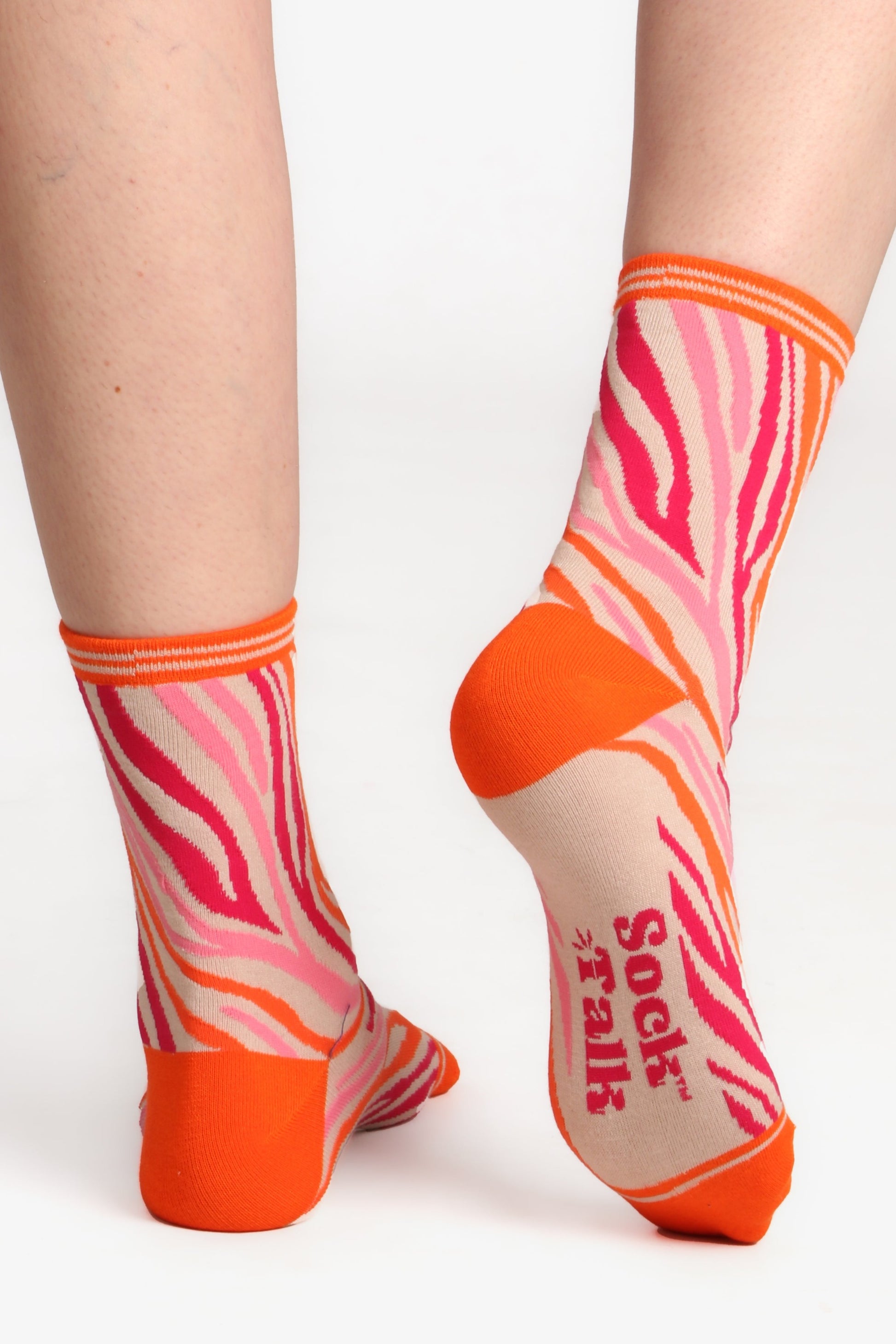 Model wearing bamboo zebra print socks. Posed with feet facing away from camera to show sole of sock which has sock talk logo 