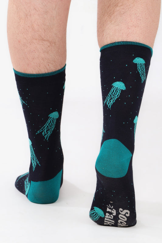 Men's feet walking away from camera wearing sock talk jellyfish fish themed bamboo socks. Socks are blue toned. Walking away shows sock talk logo on sole of socks