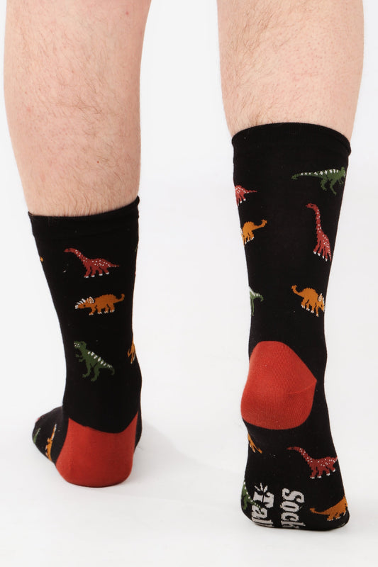 Men's feet walking away from camera wearing sock talk bamboo socks in dinosaur print. The sock are black with different dinosaurs printed all over. Image highlights contrasting colour heel and sock talk logo on sole