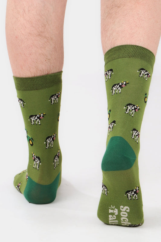 Men's tractor and cow print bamboo socks in shades of green. Men's feet walking away from camera to show sock talk logo on sole of sock