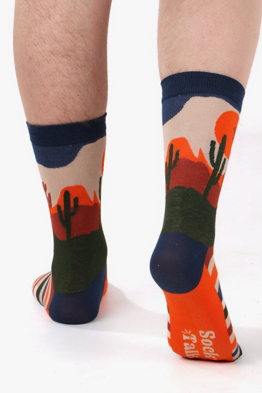 Male feet walking away from camera wearing wild west cactus themed bamboo socks in orange, blue and green tones