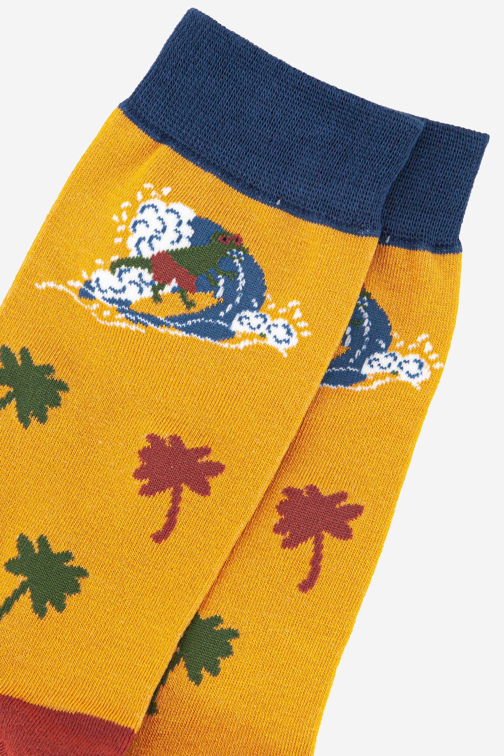 close up of the surfing dinosaur and palm tree design on the yellow and navy blue bamboo socks
