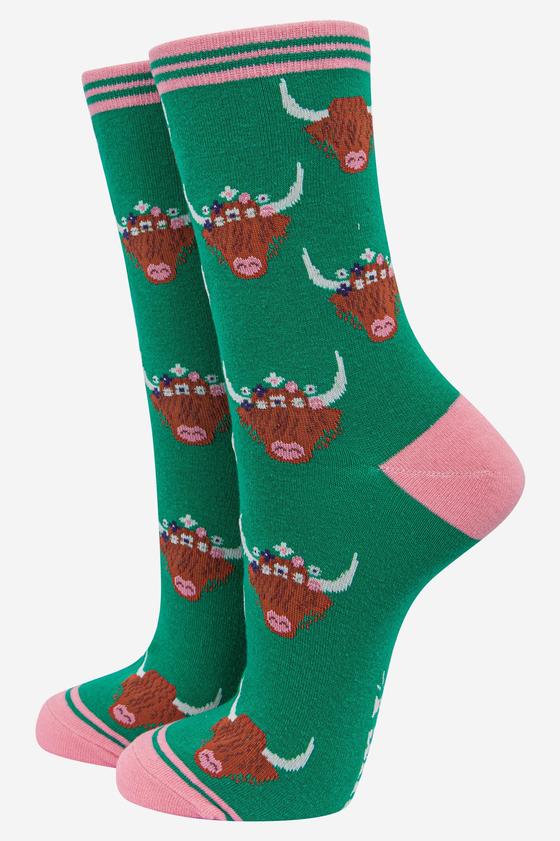 green bamboo socks with pink heel, toe and trim with an all over pattern of brown highland cow faces with horns the cows are wearing floral wreaths as crowns