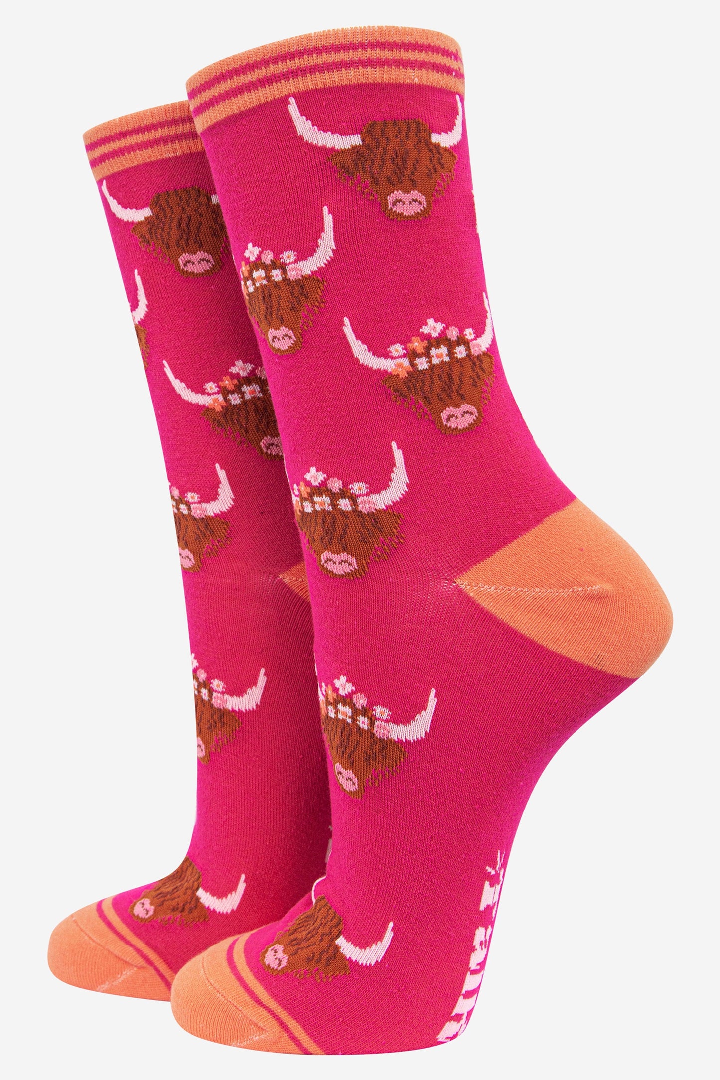 fuchsia pink bamboo socks with coral heel, toe and trim with an all over pattern of brown highland cow faces with horns the cows are wearing floral wreaths as crowns