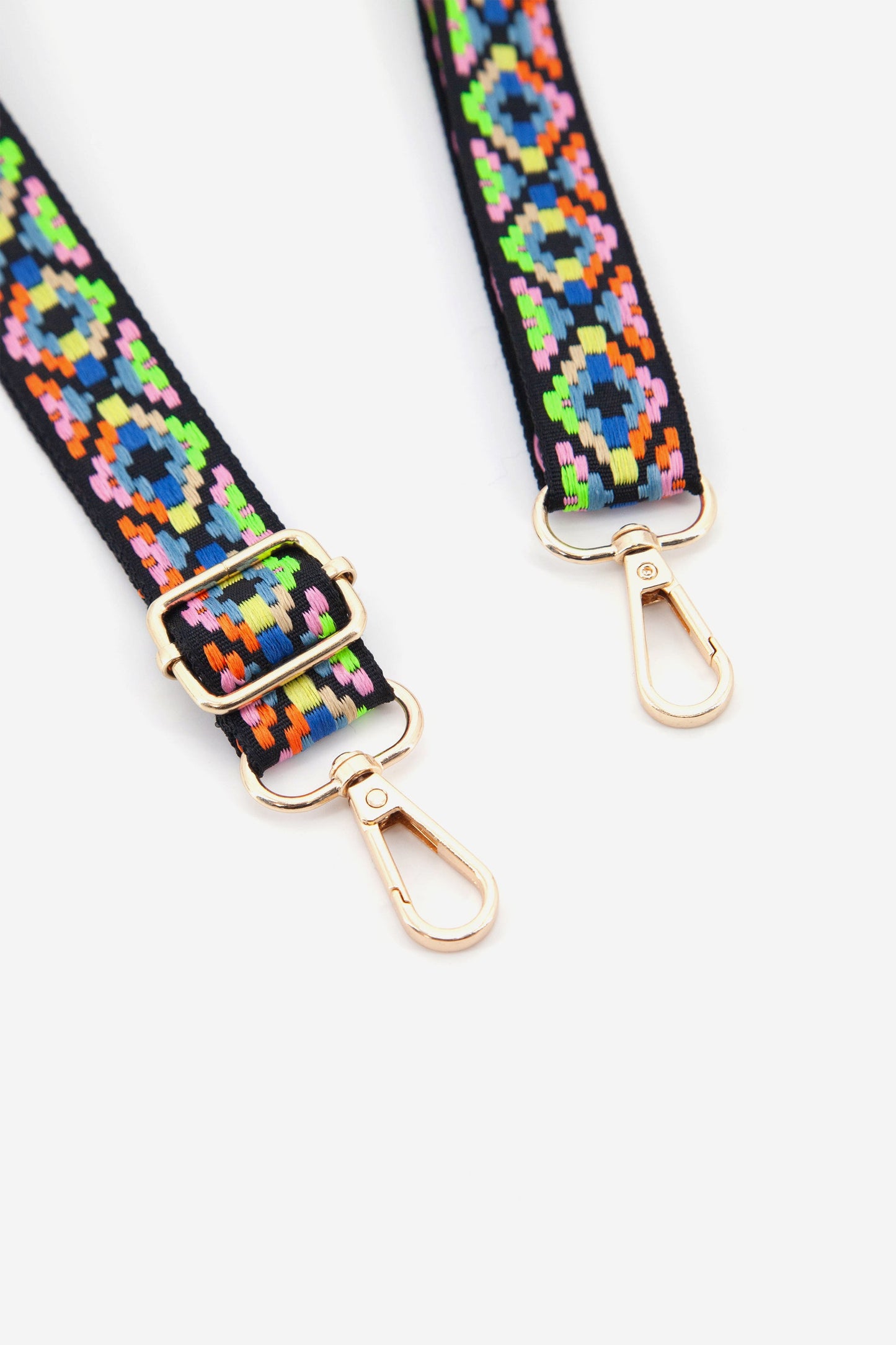 close up of the multicoloured geometric pattern bag strap and the gold clip on snap hook attachments