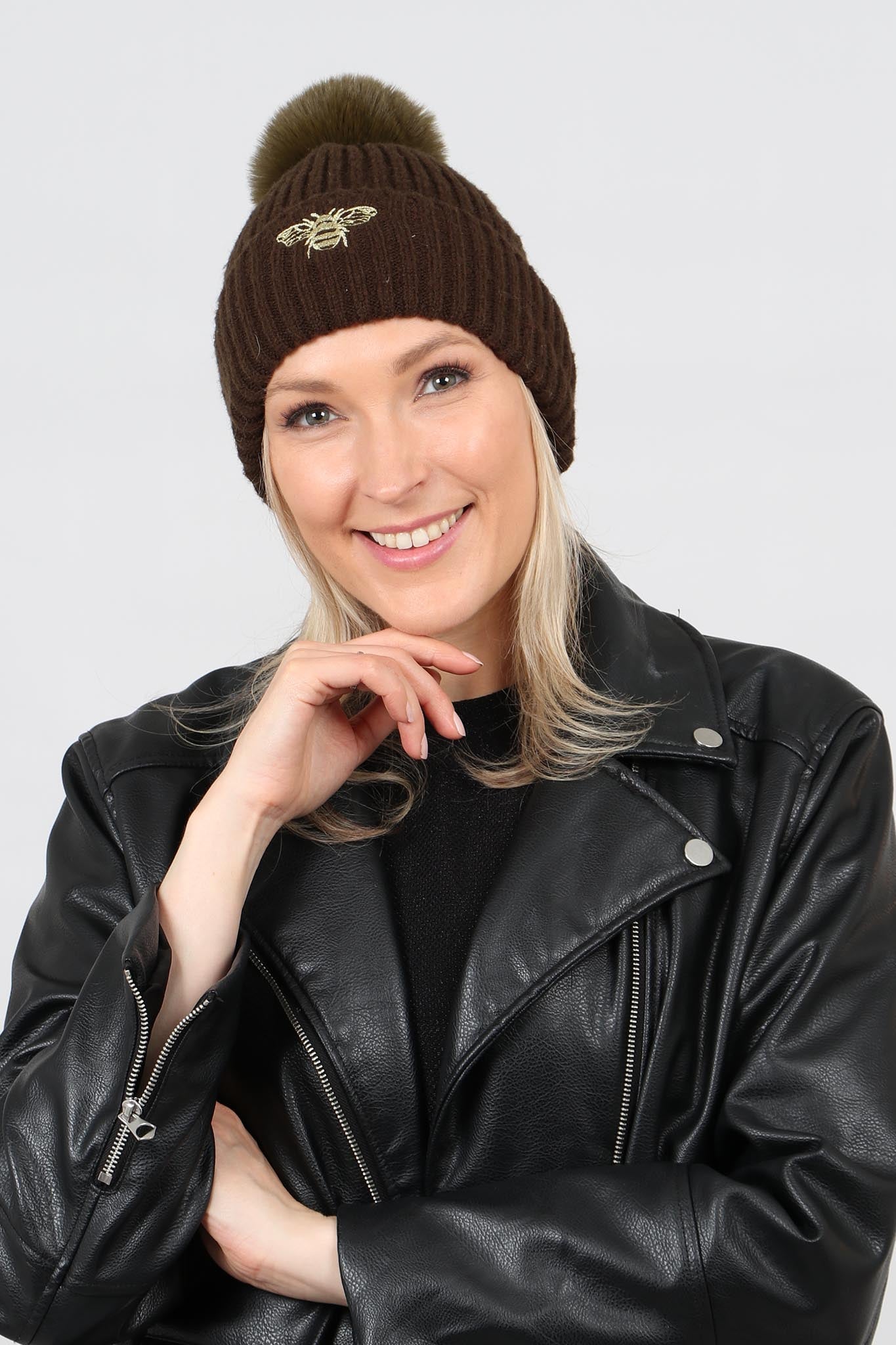 model wearing a khaki green pom pom hat with an embroidered gold bee motif on the front