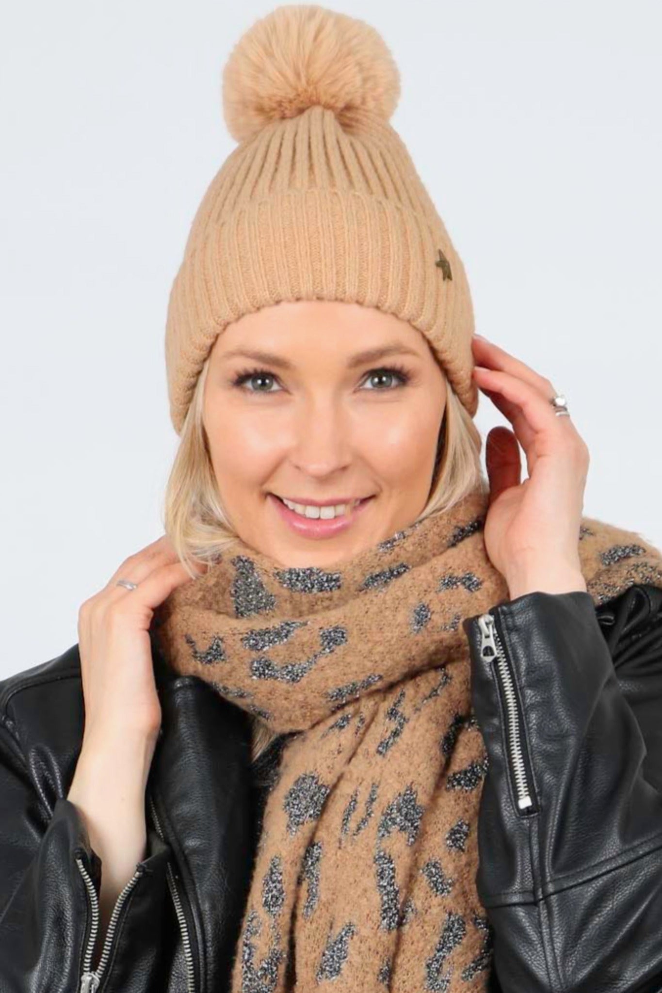 model wearing a camel coloured winter pom pom hat with a metal gold star motif on the rim